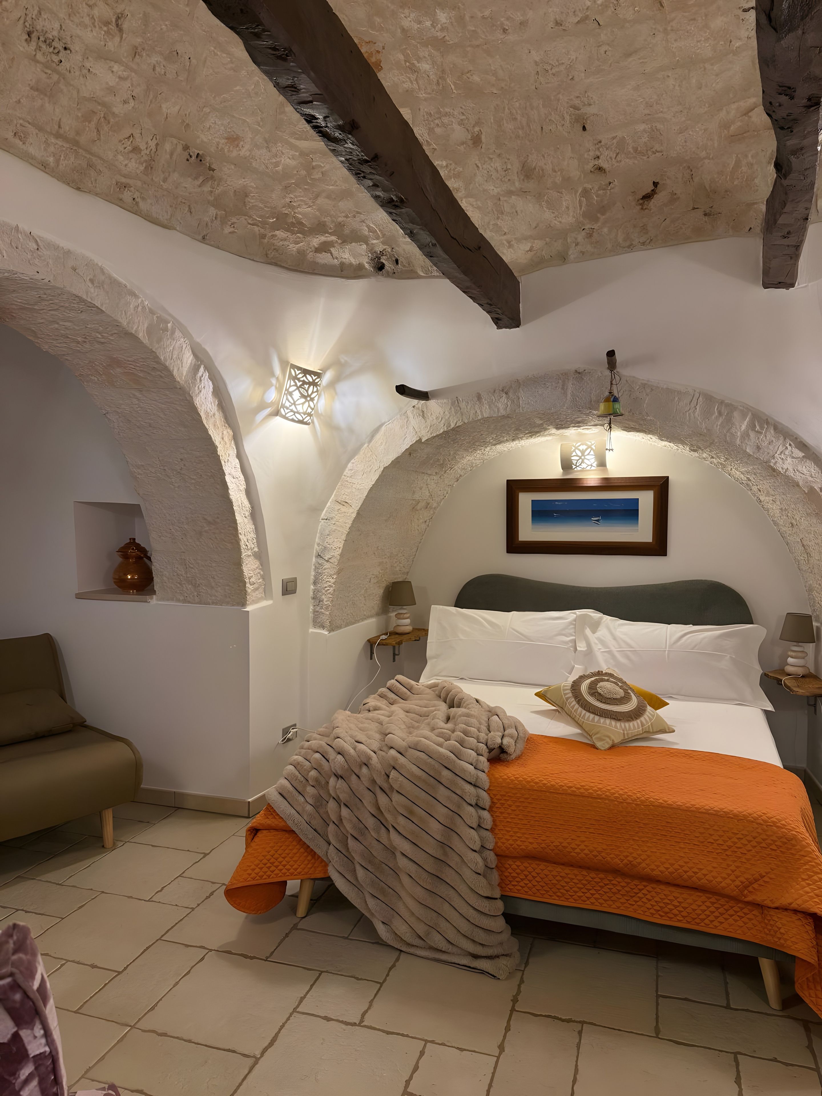 Een slaapkamer met een bed, nachtkastje, lamp, wandplank en een decoratief object.