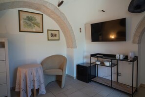 A room with a TV mounted on the wall, a small table with a tablecloth, a chair, and a cabinet with shelves. - Room 'Perla' with Shared Pool, Shared Terrace and Wi-Fi (Locorotondo)
