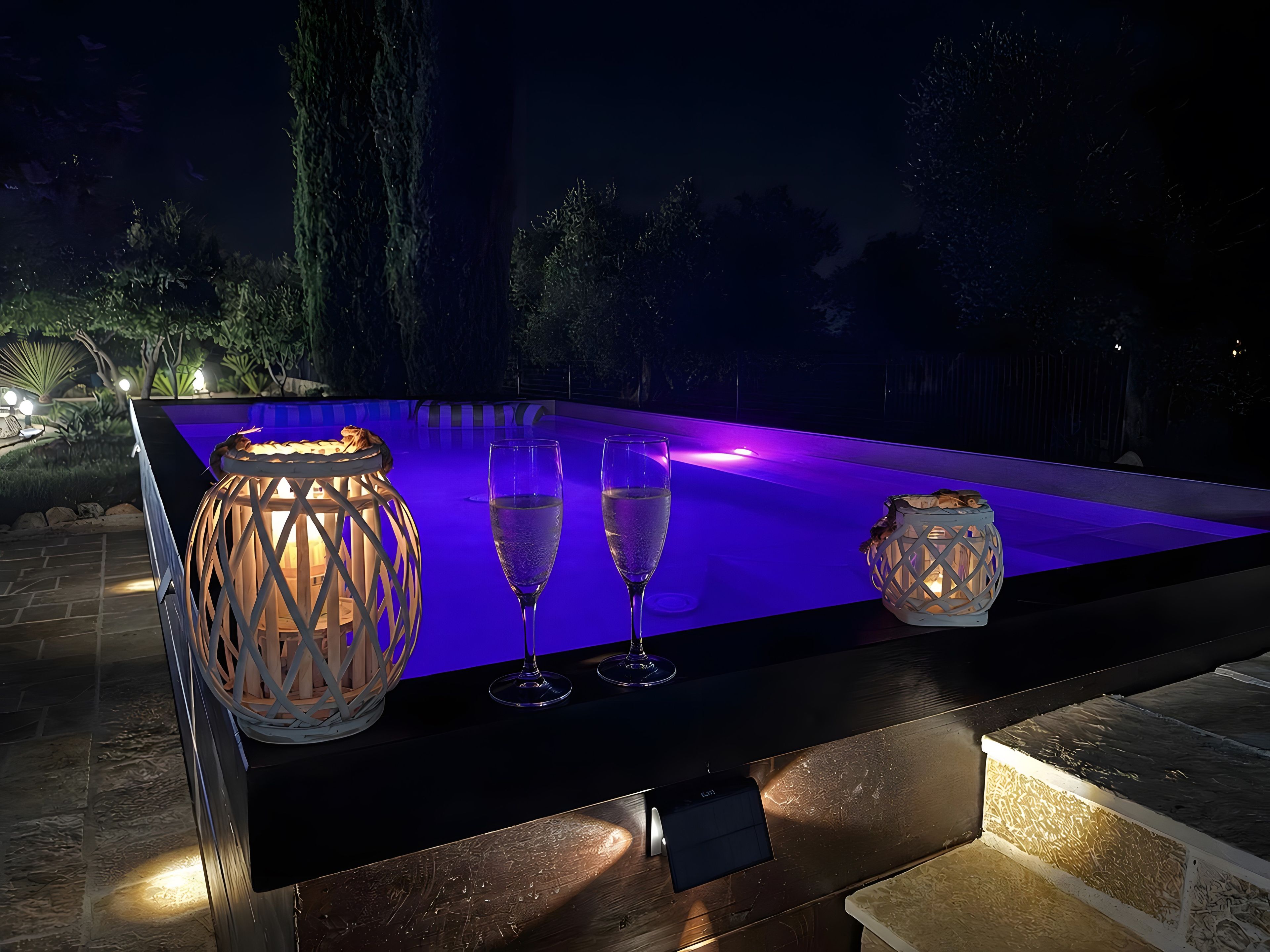 An outdoor pool area with a table, two glasses, and two lanterns.