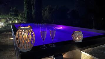 An outdoor pool area with a table, two glasses, and two lanterns.
