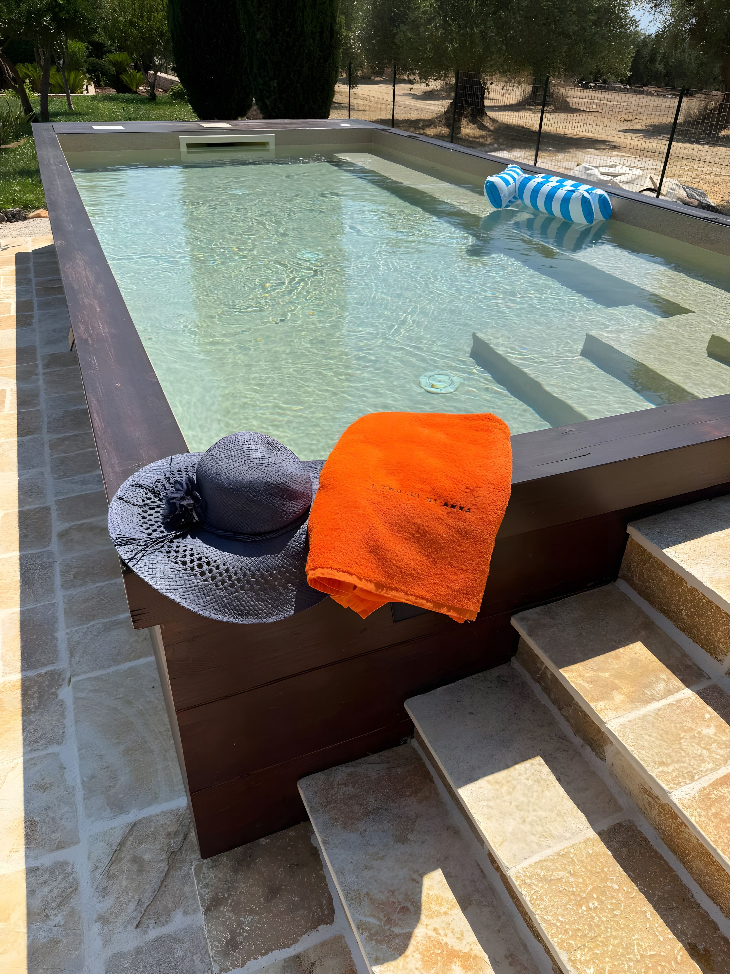 Een bubbelbad met een handdoek en een hoed op de rand, omgeven door stenen trappen en een hek.