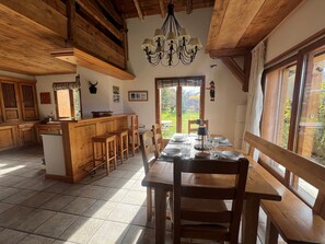 Eine geräumige Küche mit Holzschränken, eine Essecke mit Tisch für vier Personen und ein großes Fenster mit Blick ins Freie.