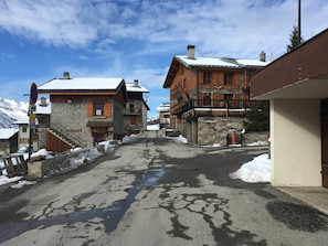 A snow-covered street with traditional wooden buildings, a clear sky, and a sign indicating no parking. - Typical Chalet 6 Rooms, Garden, 8 Pers (Saint-Martin-de-Belleville)