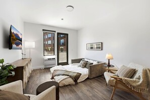A modern bedroom with a bed, a sofa, a desk, and a window with a view of buildings. - Pioche Basecamp | Deer Valley + Mountain Views (Park City)
