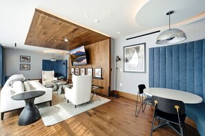 A modern living room with a wooden ceiling, a large flat-screen TV, a blue accent wall, and a dining area with a round table and chairs. - Pioche Basecamp | Deer Valley + Mountain Views (Park City)
