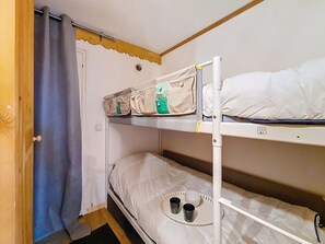 A bunk bed with a headboard, a door with a curtain, and a small table with cups and a bowl. - Studio with mountain view - 3 guests (Les Menuires)