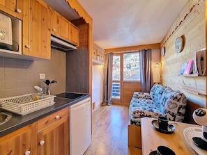 A compact kitchen with wooden cabinets, a dishwasher, and a window with curtains. - Studio with mountain view - 3 guests (Les Menuires)