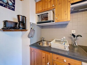 A kitchen with wooden cabinets, a microwave, a sink, and a kettle. - Studio with mountain view - 3 guests (Les Menuires)