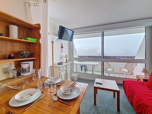 Ein Essbereich mit einem Holztisch, gedeckt für vier Personen, einem an der Wand montierten Fernseher und einem Balkon mit Aussicht.
