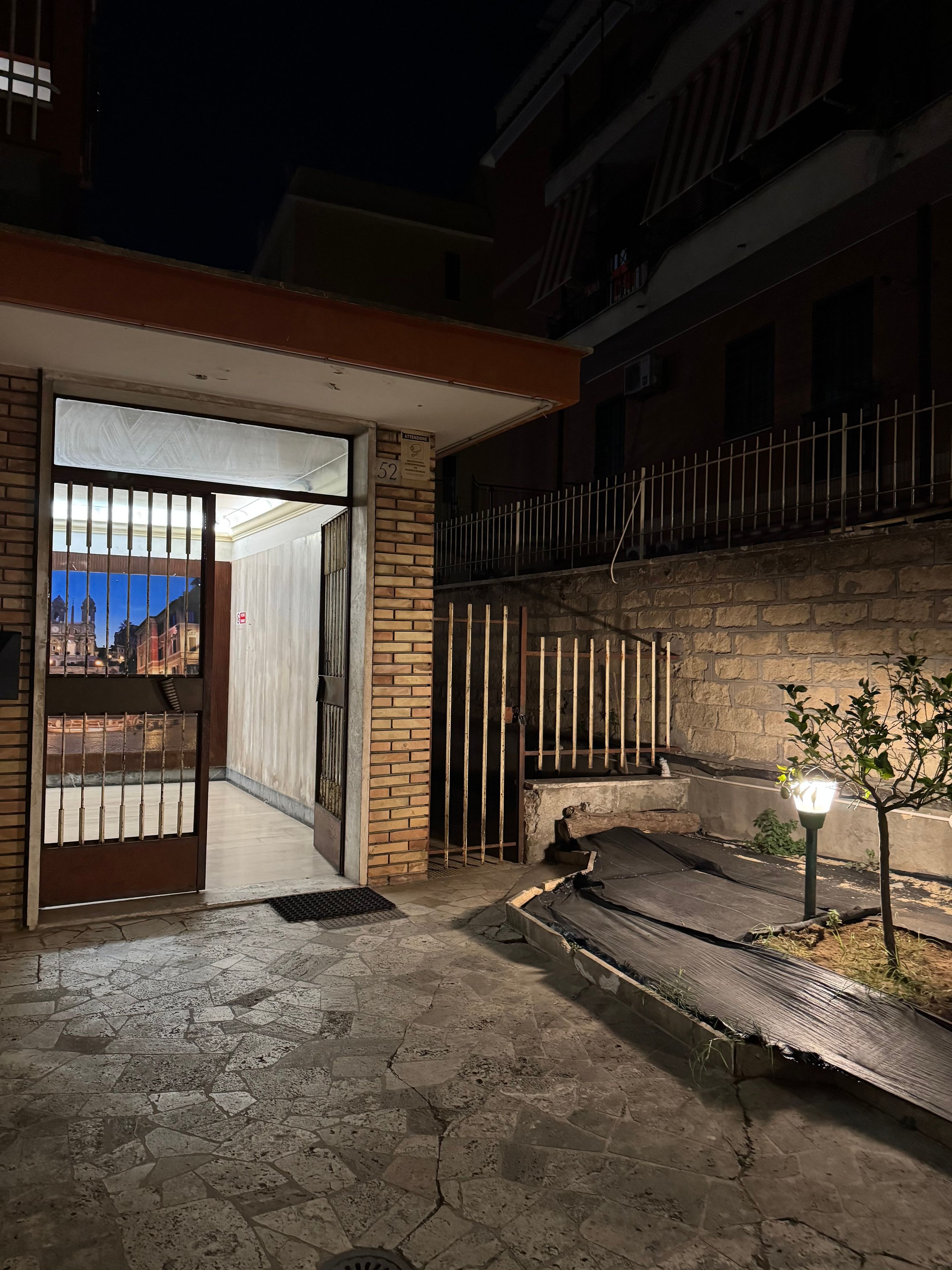 A gated entrance to a building with a tiled patio area and a small tree.