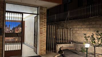 A gated entrance to a building with a tiled patio area and a small tree.