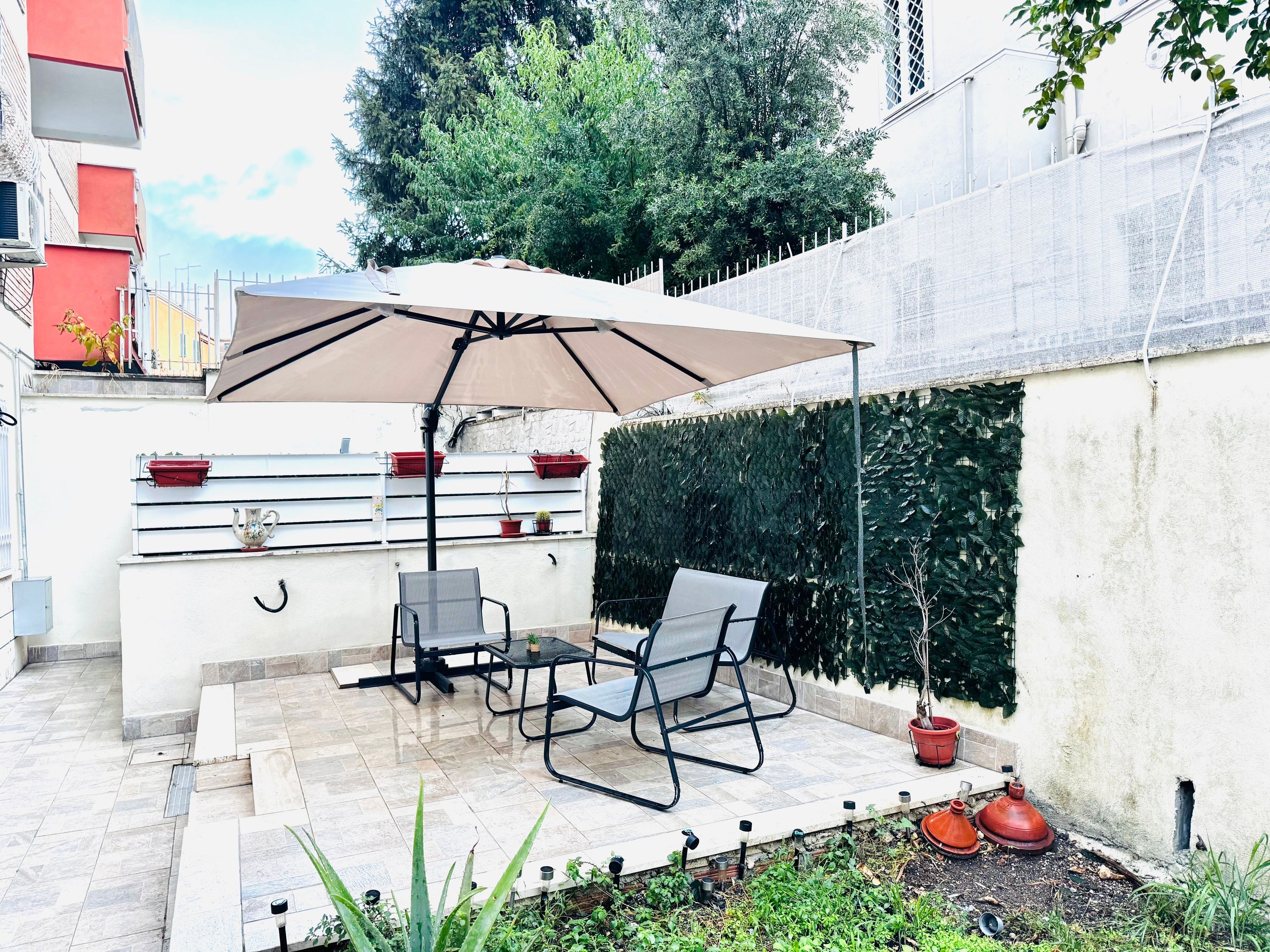 Une terrasse extérieure avec une table et des chaises, un grand parasol et un jardinier mural.