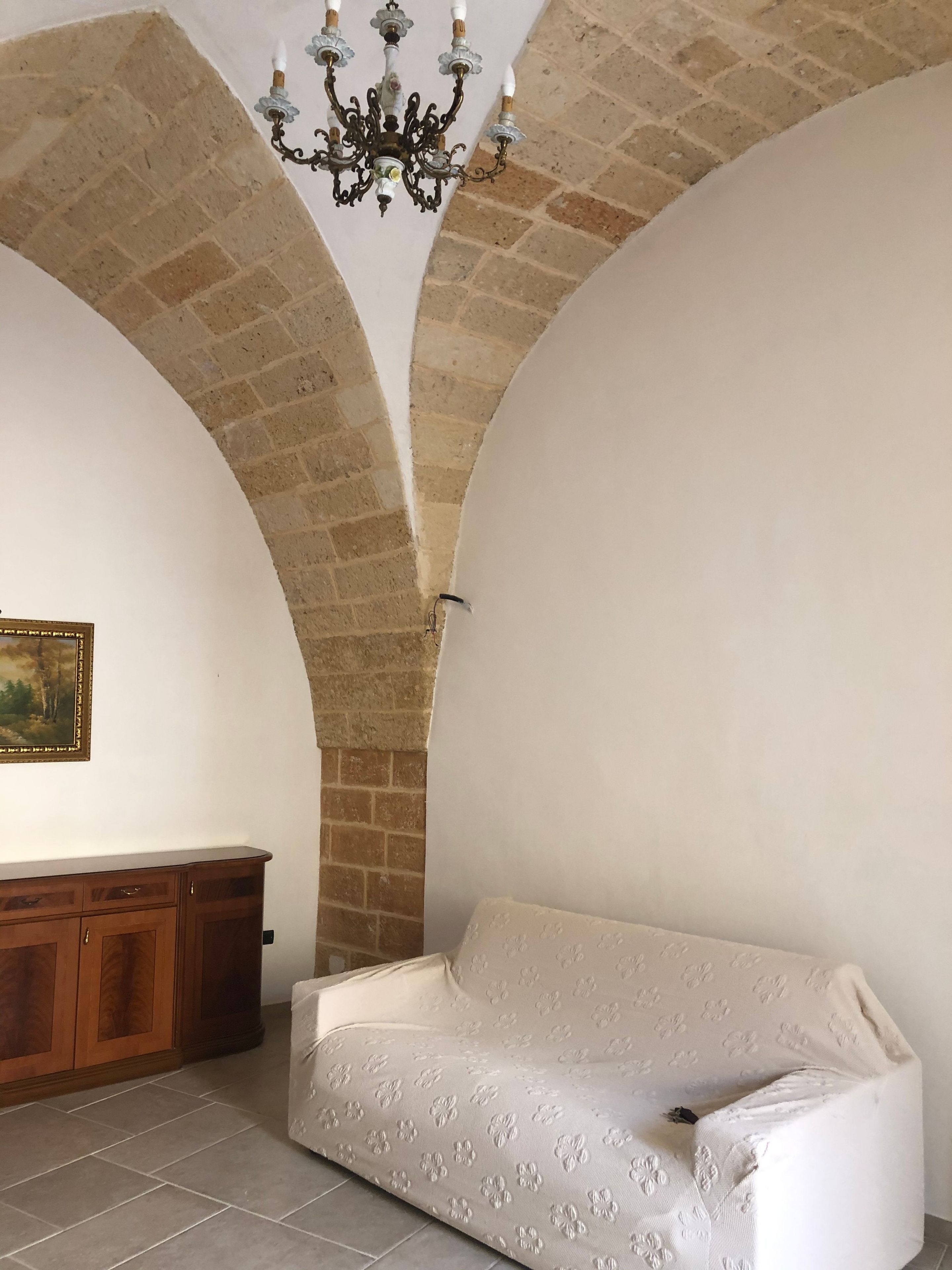 Una habitación con un sofá blanco, un armario de madera y una araña.