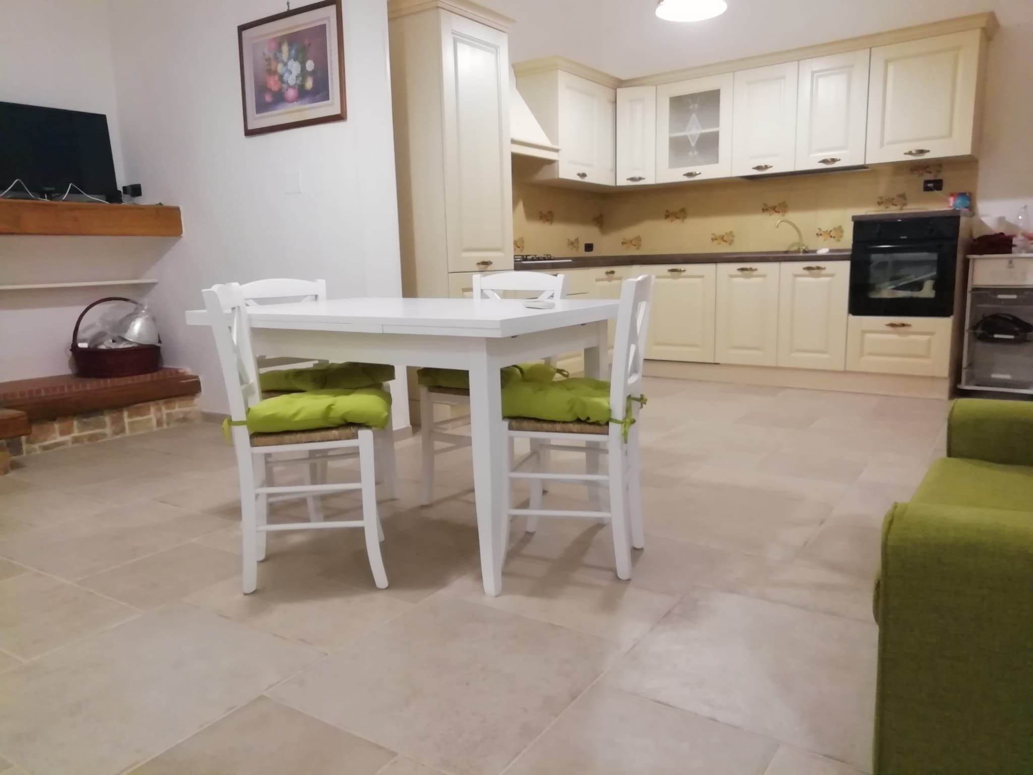 A dining area with a white table and chairs, a kitchen with white cabinets, and a green sofa.
