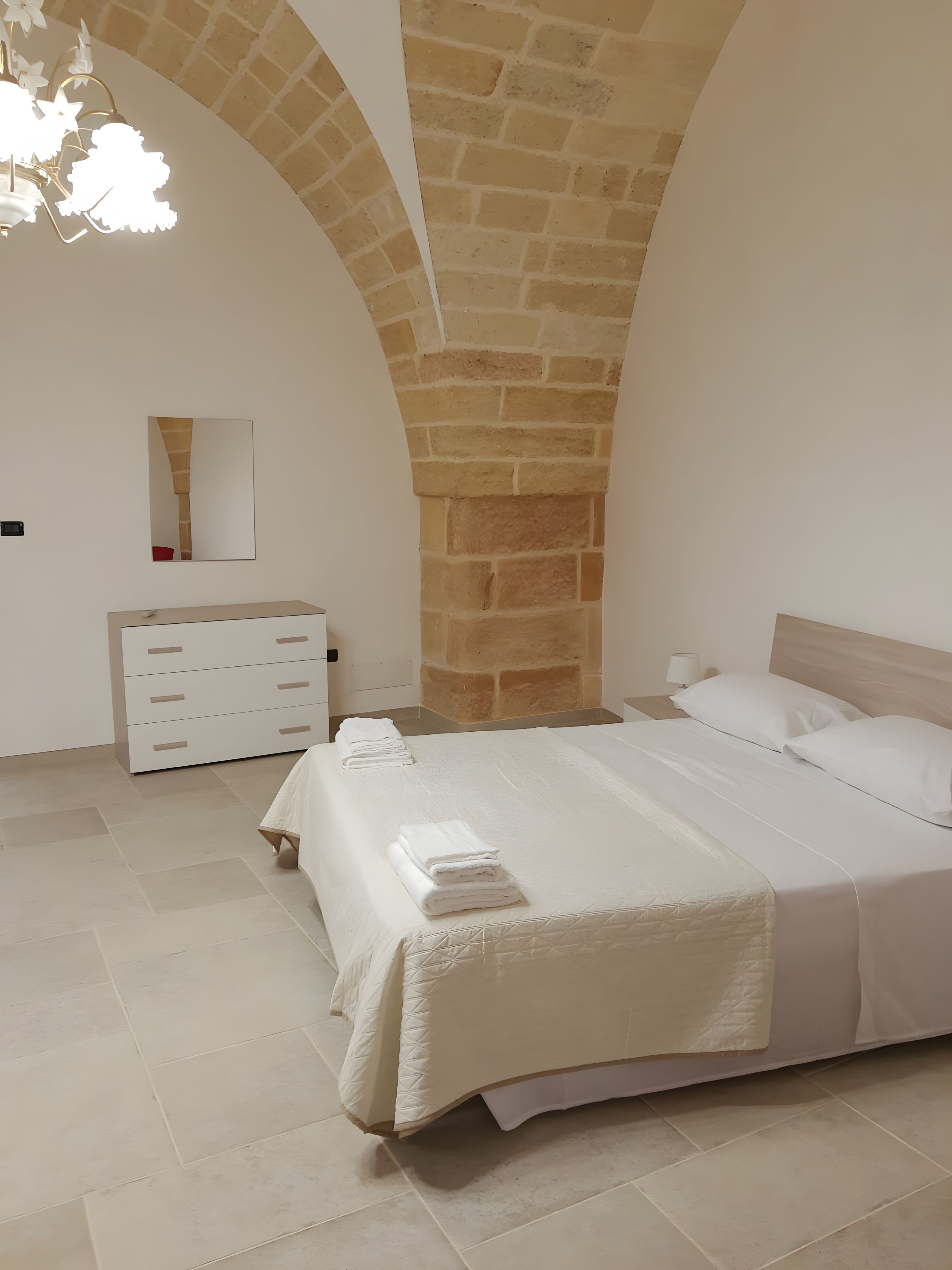 Une chambre à coucher avec un lit, une commode, un miroir et un lustre.