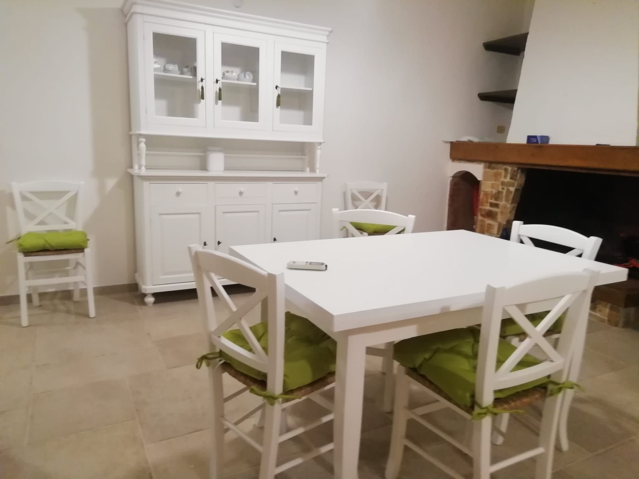 A dining area with a white table and chairs, a white cabinet with glass doors, and a fireplace.