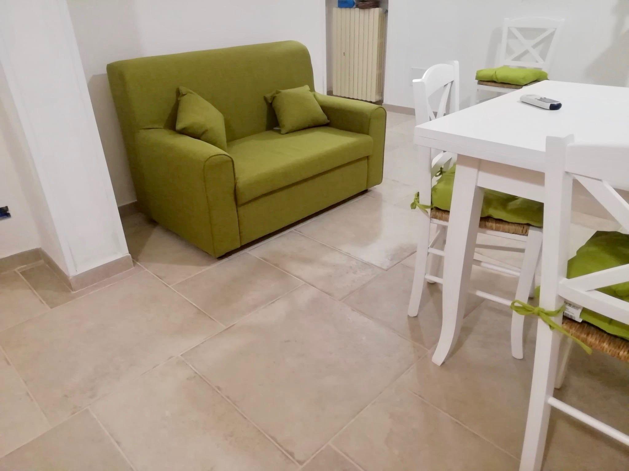 A room with a green sofa, a white table, and a chair.