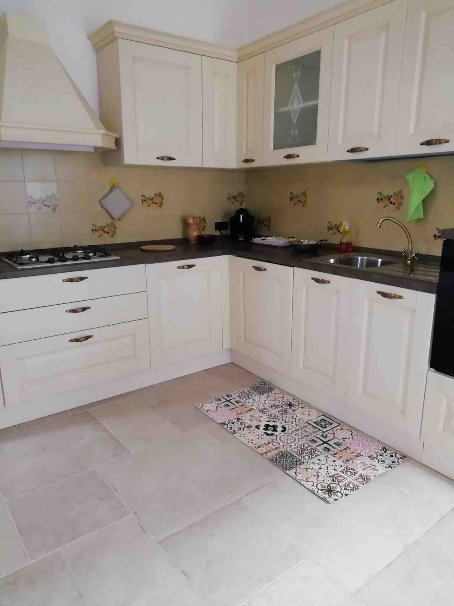 A kitchen with white cabinets, a gas stove, a sink, and a patterned rug.