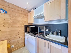 A compact kitchen with wooden cabinetry, a built-in microwave, a dishwasher, and a sink. - Pleasant apartment at the foot of the slopes - 4 guests (Les Menuires)