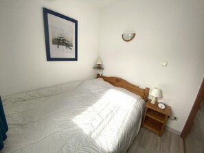 A single bed with a wooden headboard, a bedside table with a lamp, a wall-mounted light, and a framed picture. - Apartment at the foot of the slopes - 6 guests (Morillon Village)