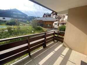 Ein Balkon mit Holzgeländer, der auf einen Wohnbereich mit Häusern und einem Berg im Hintergrund blickt.