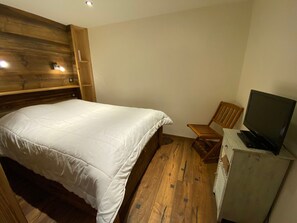 A bedroom with a bed, a wooden headboard, a chair, a television, and a desk. - Ski-in/ski-out apartment, mountain view - 4 guests (Méribel)