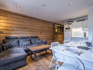 A modern kitchen with white cabinets, a dining table set with plates and glasses, and a wooden wall with a built-in bench. - Ski-in/ski-out apartment, mountain view - 4 guests (Méribel)
