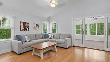A modern living room with a sectional sofa, a wooden coffee table, and large windows with blinds.
