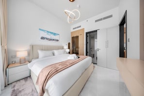 Une chambre d’hôtel moderne, dotée d’un grand lit, de tables de chevet, d’une armoire et d’une salle de bain visible à travers une porte ouverte.