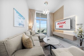 A modern living room with a sofa, a coffee table, a TV mounted on the wall, and a view of the outdoors. - StayShort - Premium 1 Bedroom in Arjan that Sleeps 4! (Arjan)