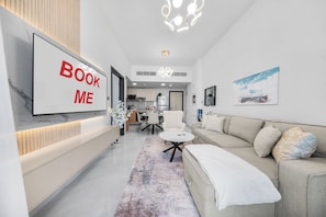 Un salon moderne avec un grand téléviseur, un canapé, un coin repas et une cuisine en arrière-plan.