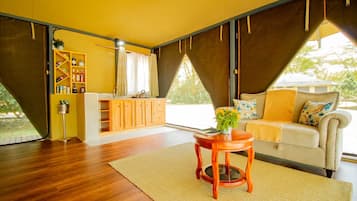 Una habitación con piso de madera, un sofá con un plaid amarillo, una pequeña mesa de madera con un florero y una zona de cocina con armarios de madera y una lámpara colgante.