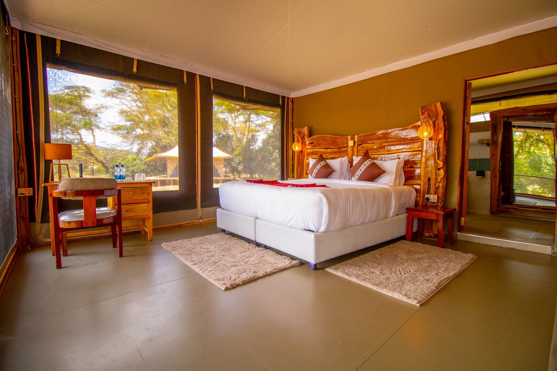 A bedroom with a large bed, wooden headboard, bedside tables, a nightstand, and a view of trees through the window.