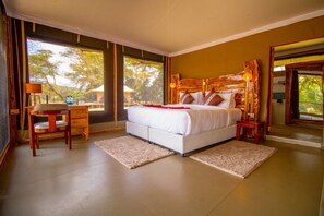 A bedroom with a large bed, wooden headboard, bedside tables, a nightstand, and a view of trees through the window.
