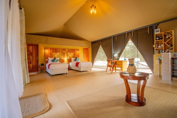 A spacious living area with a high ceiling, a wooden headboard, a round wooden table, and a bookshelf with various items.