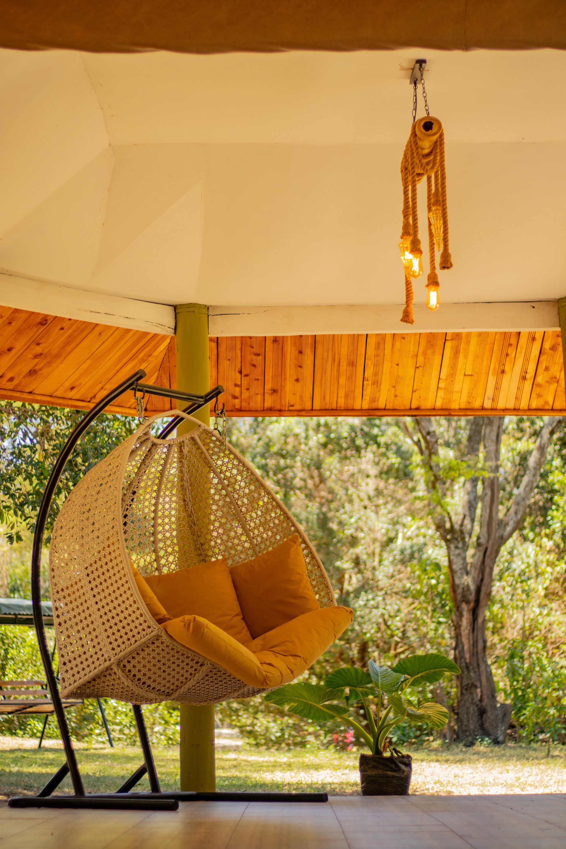 Una silla colgante con cojines en un espacio exterior cubierto con vistas a árboles.