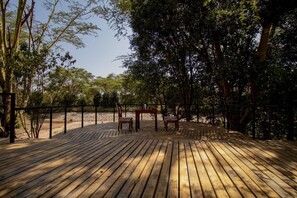 A wooden deck with chairs and tables, surrounded by trees.