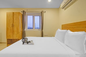 A hotel room with a bed, a wardrobe, a window with curtains, and an air conditioning unit. - Super Townhouse Whiteridge Gachibowli  (Hyderabad)