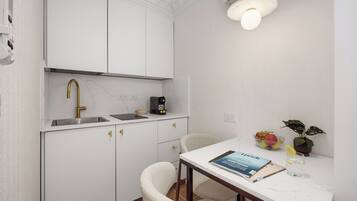 A compact kitchen with a white countertop, a gold faucet, a coffee maker, and a dining area with a chair and a table.
