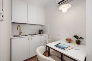 Una cocina compacta con encimera blanca, grifo dorado, cafetera y una zona de comedor con una silla y una mesa.