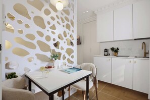 A modern kitchen with white cabinetry, a dining table with chairs, and a decorative wall with cut-out patterns. - baraca botique -hamadregot 8 (Jerusalem)