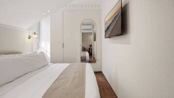 Un dormitori modern amb un llit gran, un televisió de pantalla plana penjada a la paret i un passadís que condueix a una altra habitació.