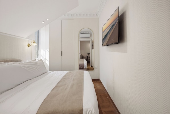 A modern bedroom with a large bed, a flat-screen TV mounted on the wall, and a hallway leading to another room. - baraca botique -hamadregot 8 (Jerusalem)