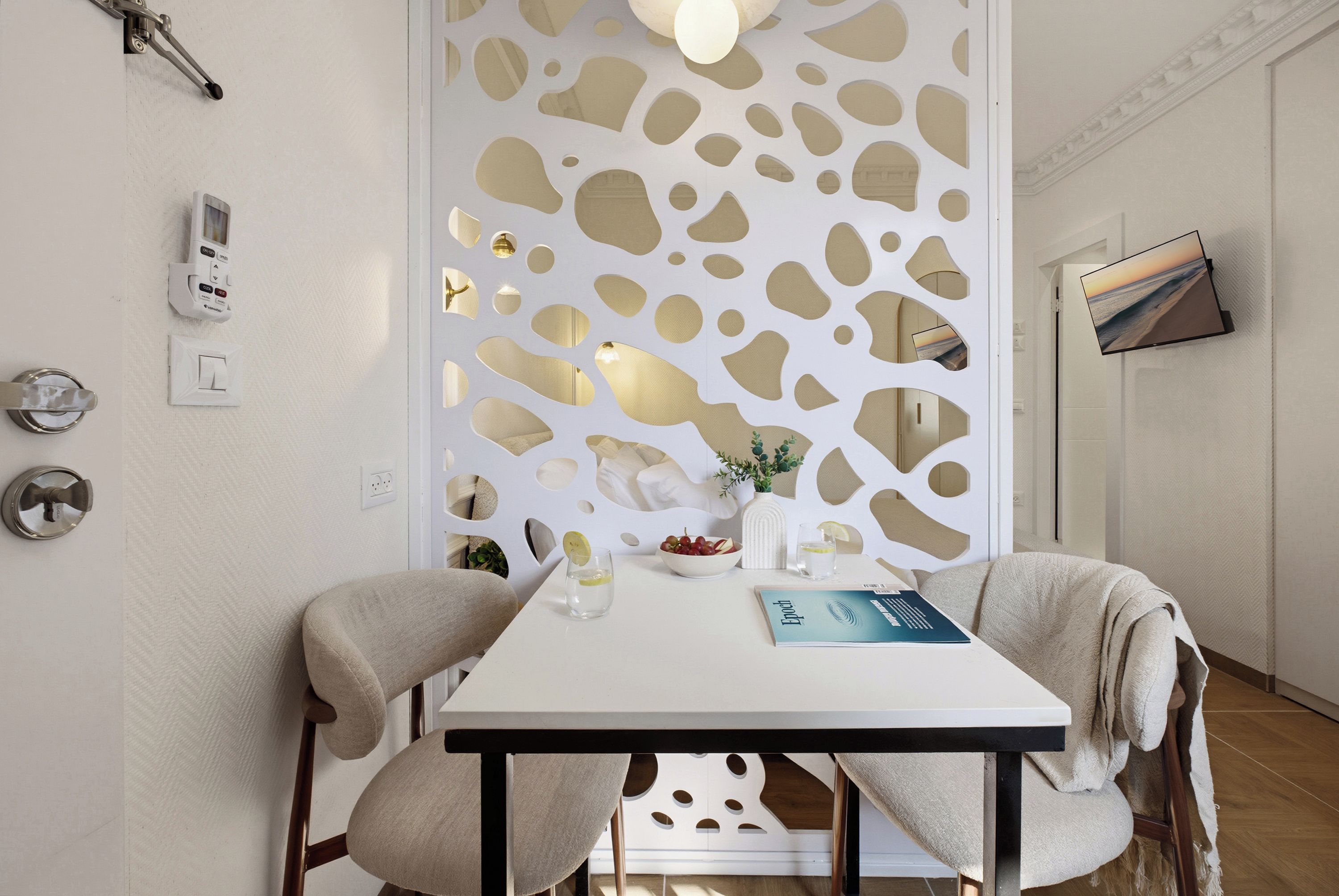 Un comedor moderno con una mesa blanca, dos sillas, un panel decorativo y un televisor de pantalla plana montado en la pared.