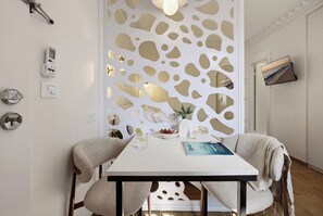 A modern dining area with a white table, two chairs, a decorative partition, and a flat-screen TV mounted on the wall. - baraca botique -hamadregot 8 (Jerusalem)