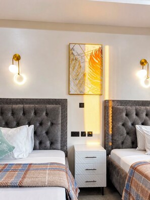 A hotel room with two beds, a nightstand, and wall-mounted lighting. - Beachfront Apartments and Suites, Nyali (Mombasa)