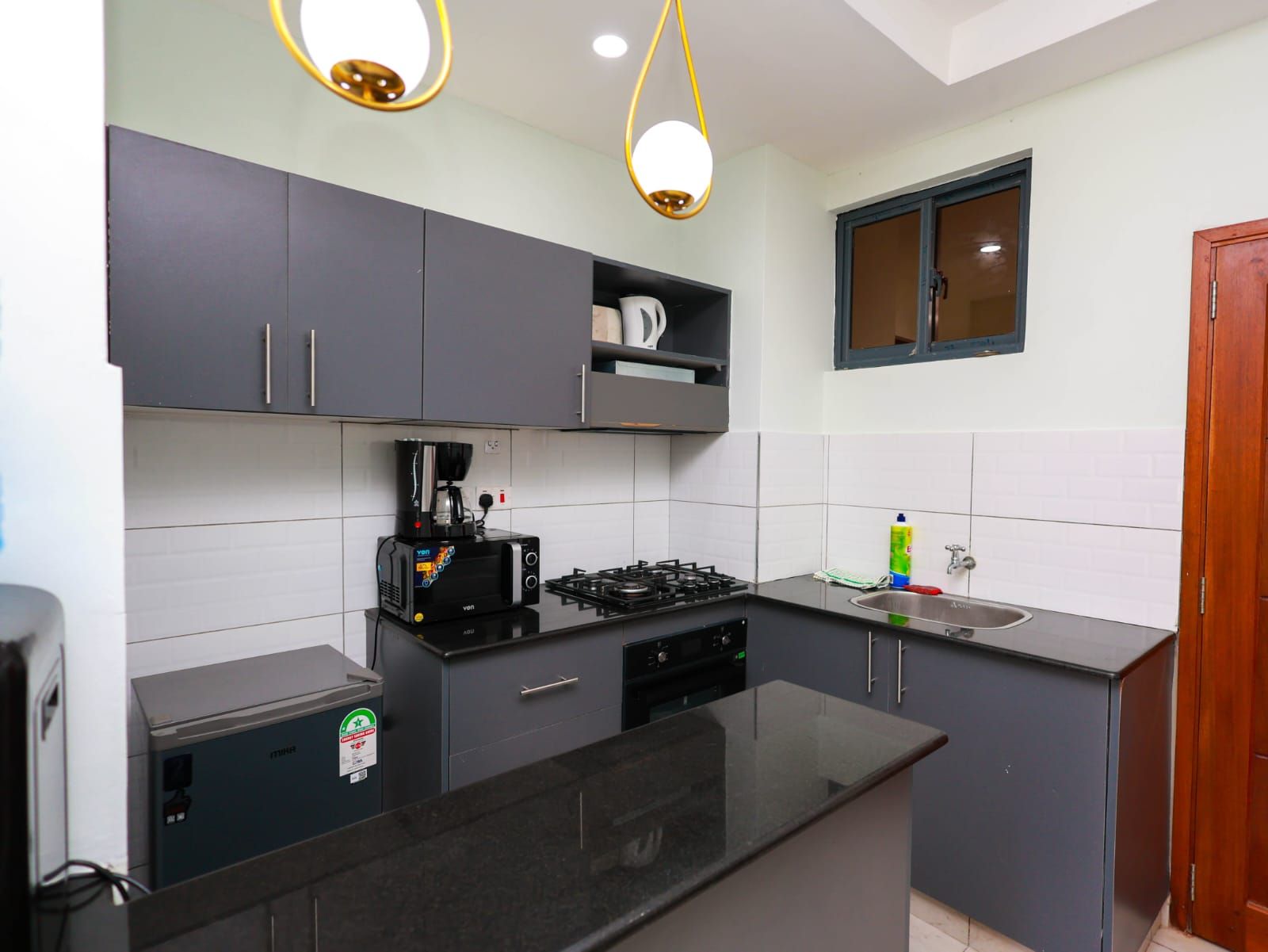Een kleine keuken met een gasfornuis, een koffiezetapparaat en een spoelbak.