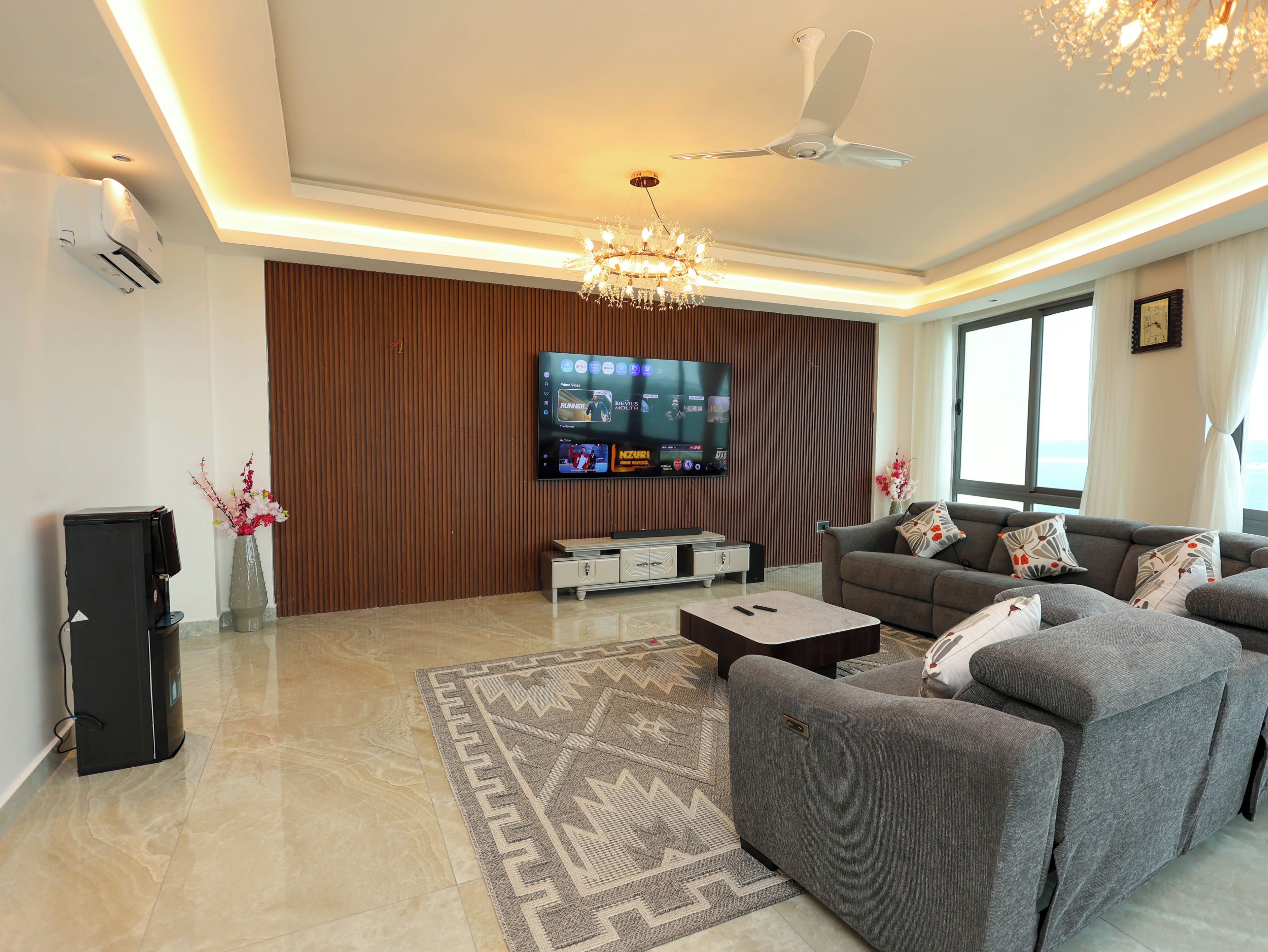 A modern living room with a flat-screen TV, a ceiling fan, and a patterned rug.