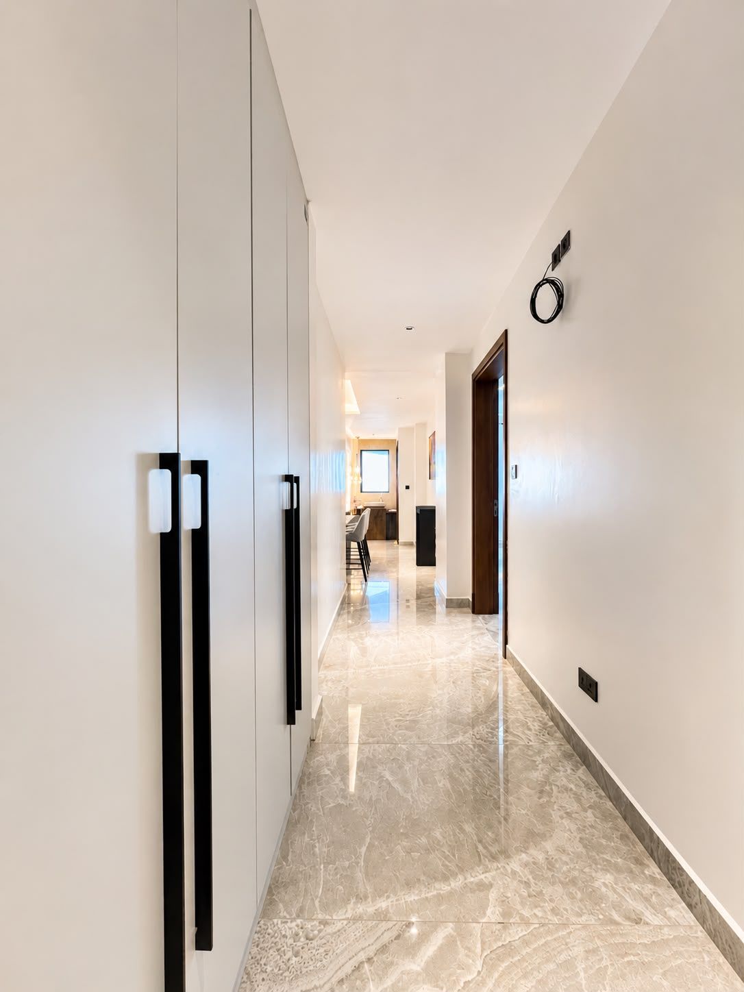 A hallway with a marble floor, a door on the right, and a view into a room with a dining area.