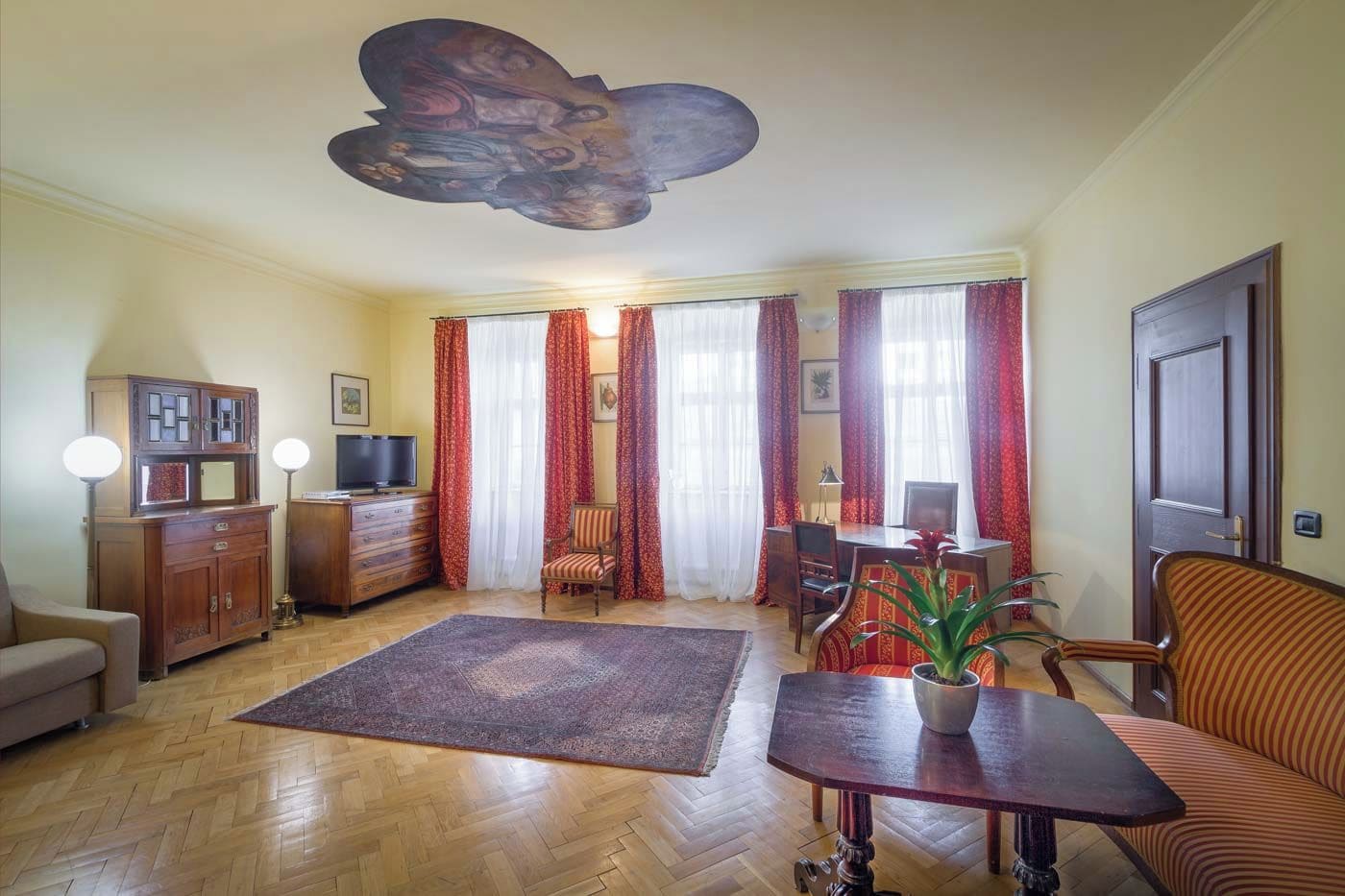 Sala de estar con piso de espiga, sofá, mesa de centro, televisor, mueble y un mural en el techo.